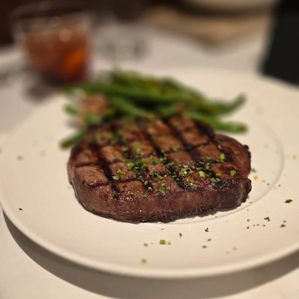 Grilled steak with grill marks, topped with herbs, served with green beans on a white plate.