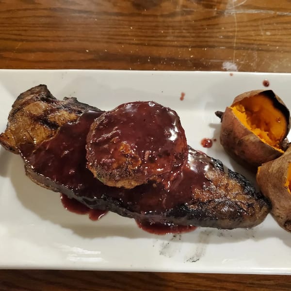 Grilled steak with a dark red sauce and a side of baked sweet potatoes on a white plate.