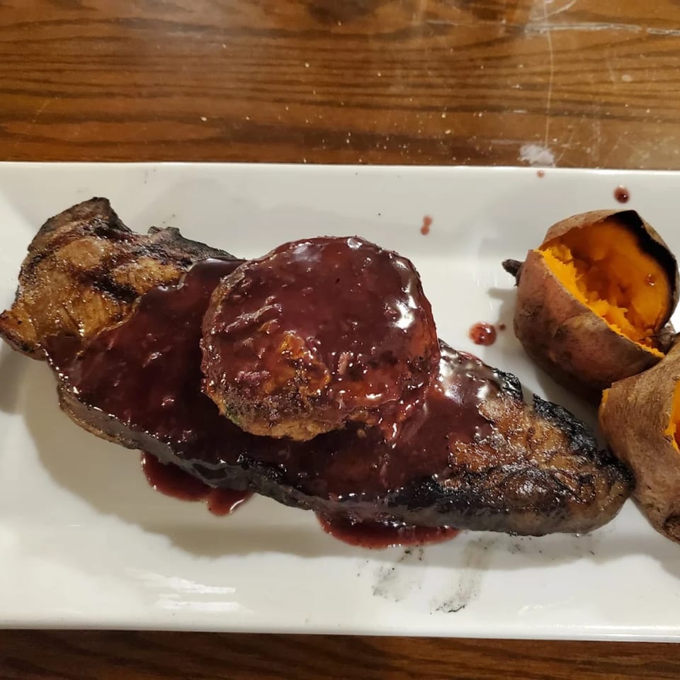 Grilled steak with a dark red sauce and a side of baked sweet potatoes on a white plate.