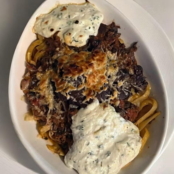 A white oval dish filled with pasta, meat, melted cheese, and two dollops of white sauce.