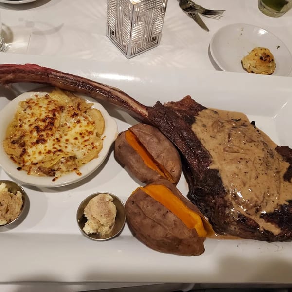 A large tomahawk steak with sauce, two baked sweet potatoes, and cheesy scalloped potatoes.