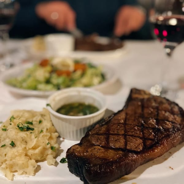 A grilled steak, mashed potatoes, green sauce, and salad on a white plate at Scratch Steakhouse.