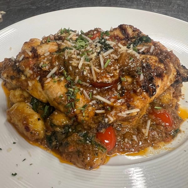 Grilled chicken breast with gnocchi, cherry tomatoes, and a rich sauce, topped with cheese and herbs.