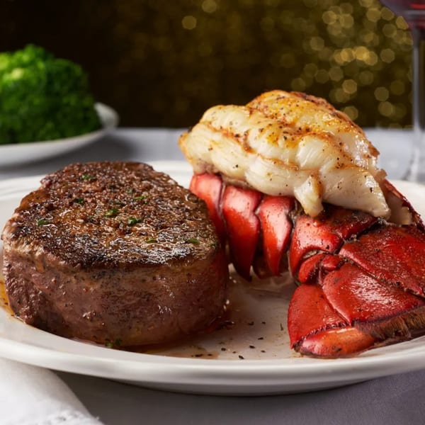Grilled steak and lobster tail with broccoli and a glass of red wine in the background.