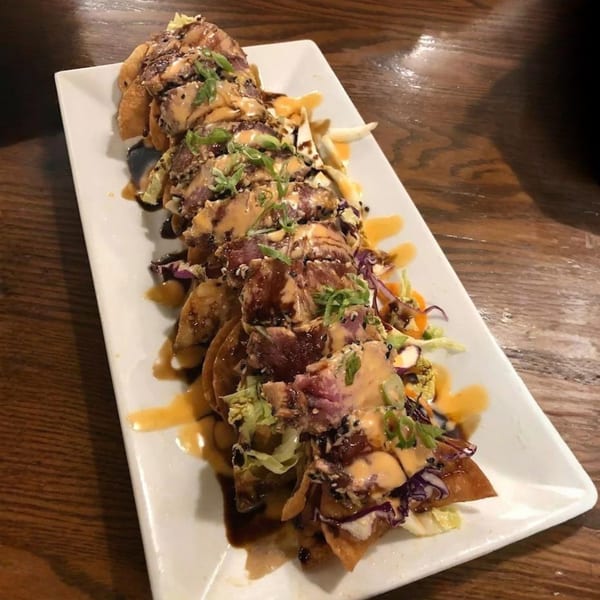 A long white plate of seared tuna nachos with sauces, sesame seeds, and green onions.
