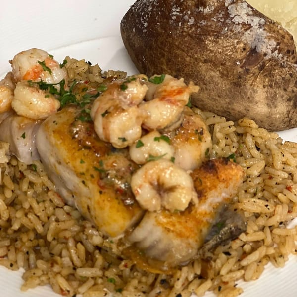 Grilled fish topped with shrimp and parsley, served with rice and a baked potato.