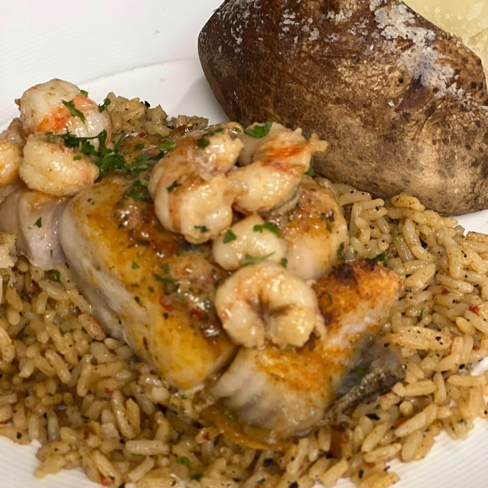 Grilled fish topped with shrimp and parsley, served with rice and a baked potato.