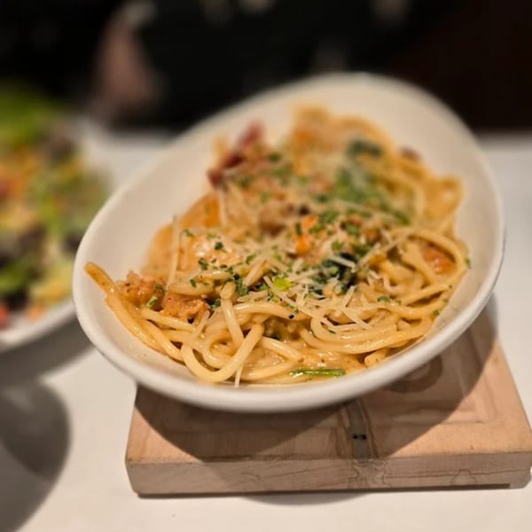 Creamy spaghetti with grated cheese and herbs in a white bowl on a wooden board.